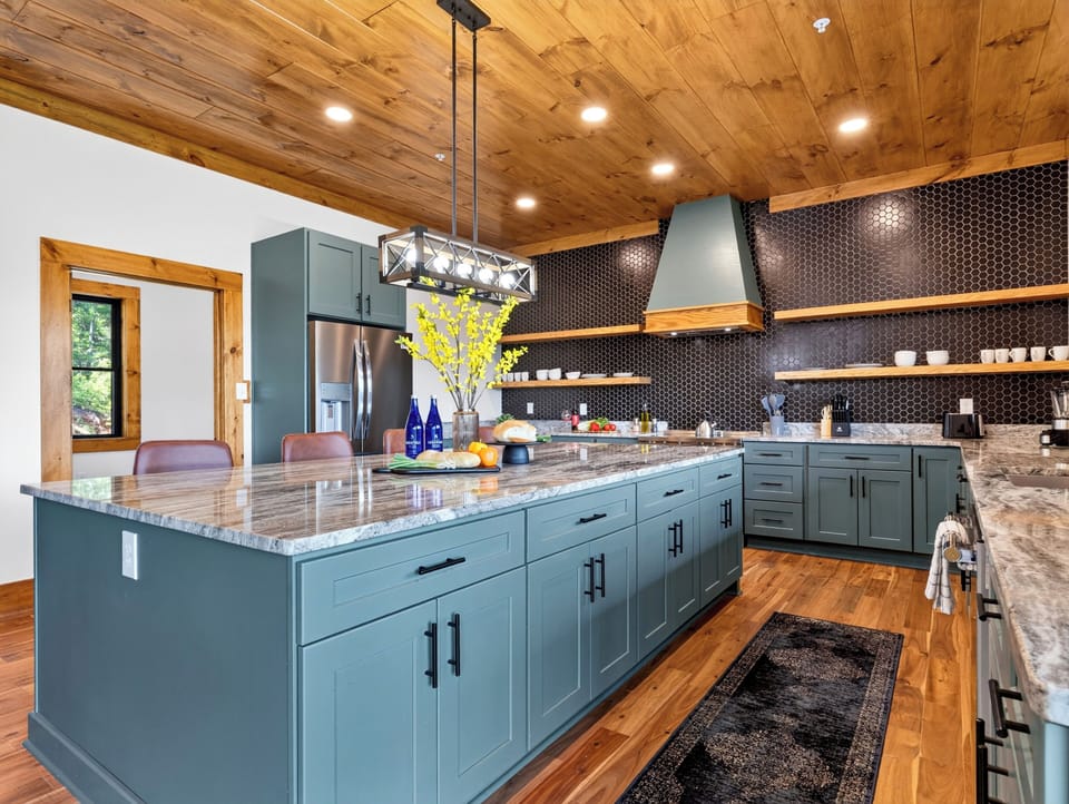 Wide-angle view of the gourmet kitchen featuring an expansive blue-green island with marble countertops. (1940)