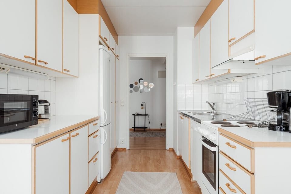 Modern galley-style kitchen with white cabinetry, wood accents and full-size appliances