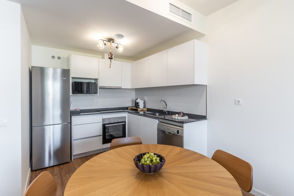 The kitchenette includes a fridge-freezer, induction hob, oven, microwave, dishwasher, kettle and coffee machine, along with essential cookware and tableware. A welcome set with coffee, tea and basic spices is also provided.