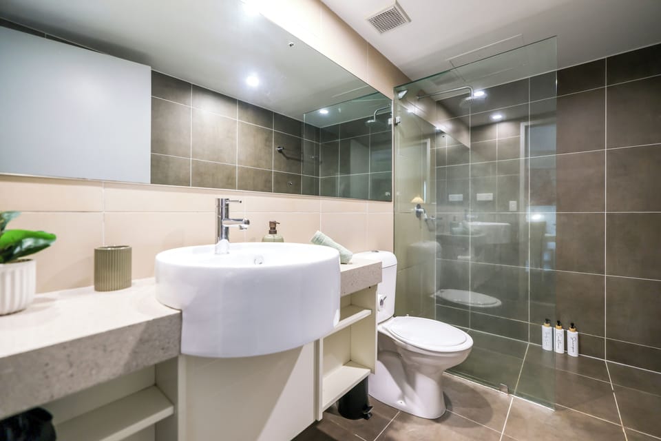 Modern bathroom featuring a stone-top vanity with a round sink, a large wall mirror, a toilet, and a glass-enclosed walk-in shower with a rainfall showerhead.