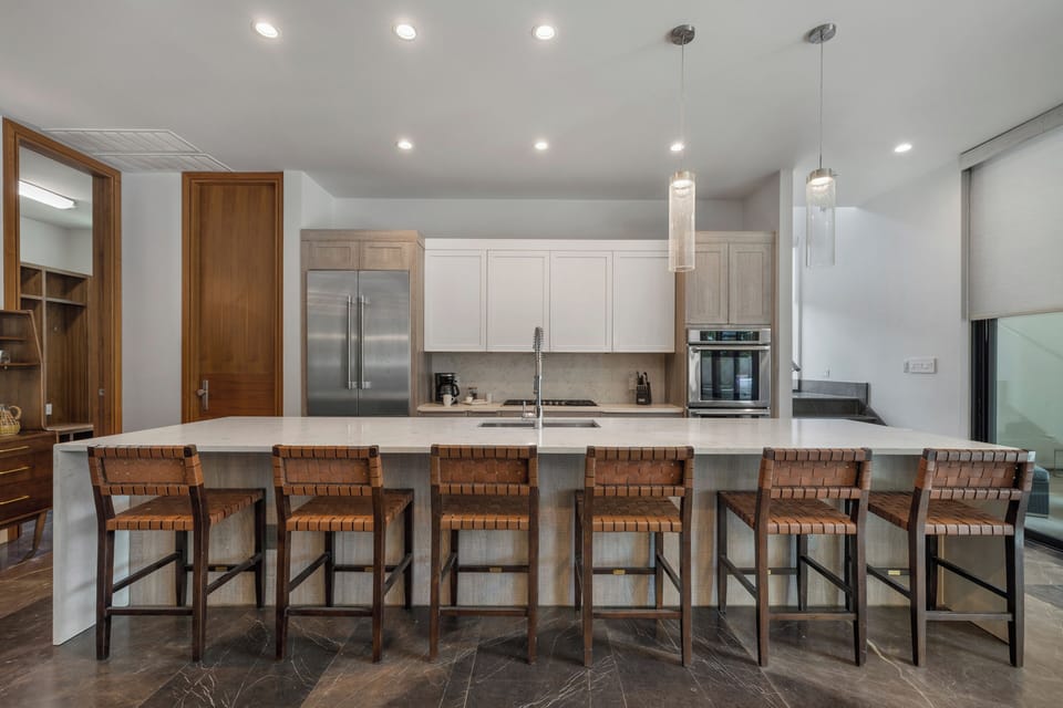 Six leather stools line the island beneath warm glass pendants.