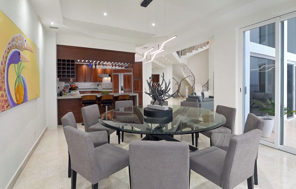 Gather around this stunning glass dining table beneath a sculptural chandelier. The open flow connects to a gourmet kitchen, while natural light spills in through floor-to-ceiling doors.
