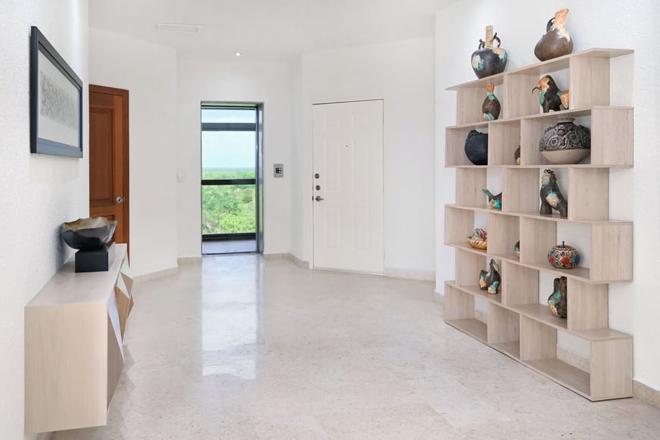 A welcoming entryway with polished floors and contemporary shelving greets you upon arrival. Natural greenery frames your first glimpse of this modern retreat, setting the tone for a stylish, serene escape.