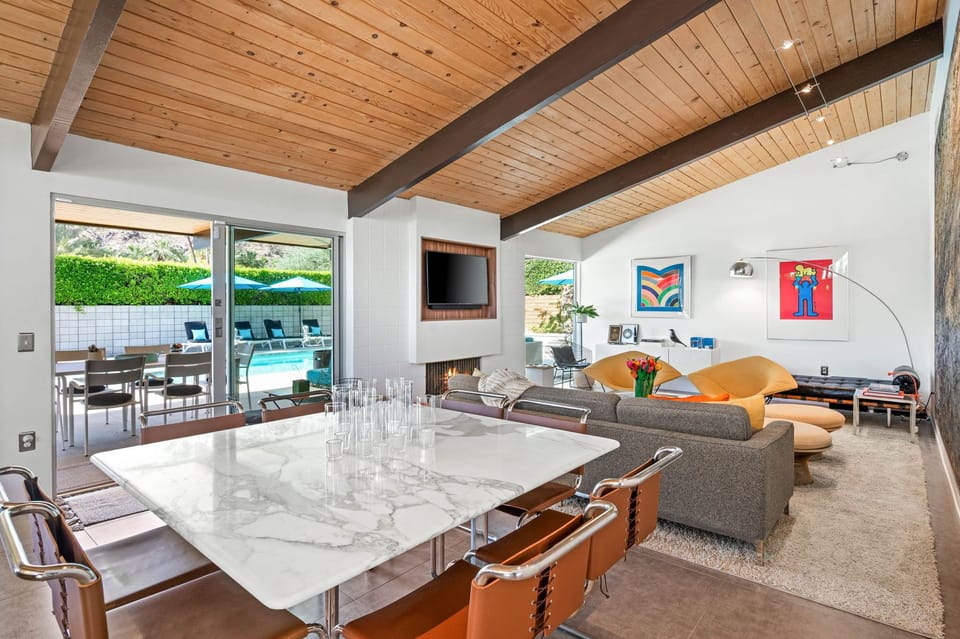 Unwind in your stylish living space where mid-century design meets modern comfort, featuring stunning pool views and warm wood-beam ceilings.