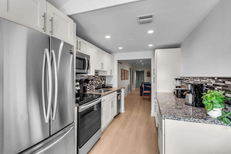 Bright kitchen with stainless steel appliances, granite countertops, and crisp white cabinetry. Fully stocked with a coffee maker and cooking essentials, opening to the living space.