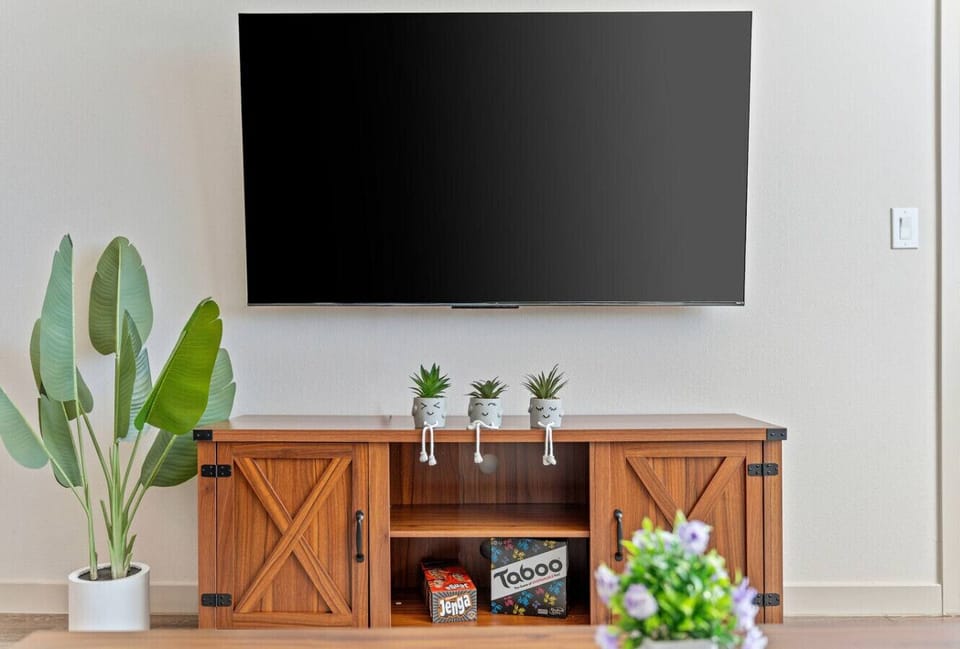 This entertainment area features a mounted flat-screen TV and a console table decorated with charming potted plants.