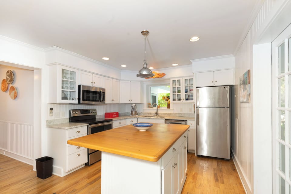 This bright, fully-equipped kitchen invites you to prepare your favorite meals with stainless appliances, ample counter space, and a charming wood-topped island at the heart of it all.