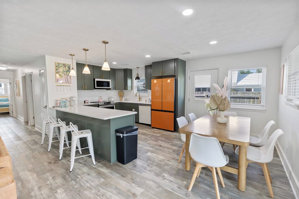 Step into your open-concept kitchen and dining area, where deep green cabinetry and modern brass fixtures create a sophisticated space for cooking and gathering. The island invites morning coffee while sunlight streams through bright windows.