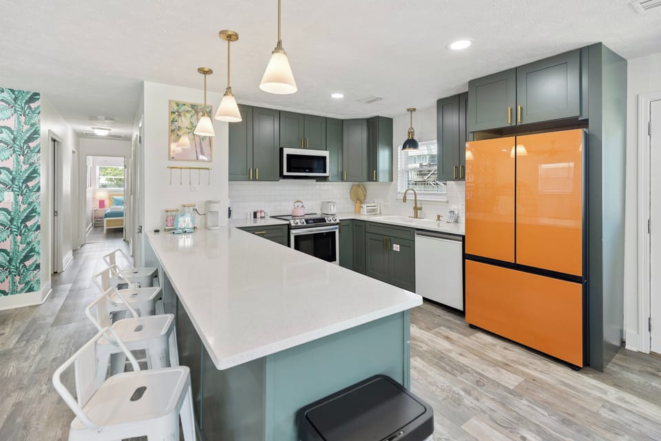 Your modern chef's kitchen awaits, featuring rich forest-green cabinetry, a bright center island with seating, and stainless-steel appliances—all bathed in natural light.