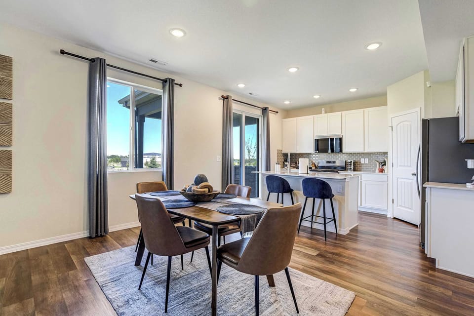 This open layout connects dining and kitchen effortlessly, with a farmhouse style table and bench seating. White shaker cabinetry and a French door refrigerator are visible in the background, hinting at the well equipped kitchen ahead.