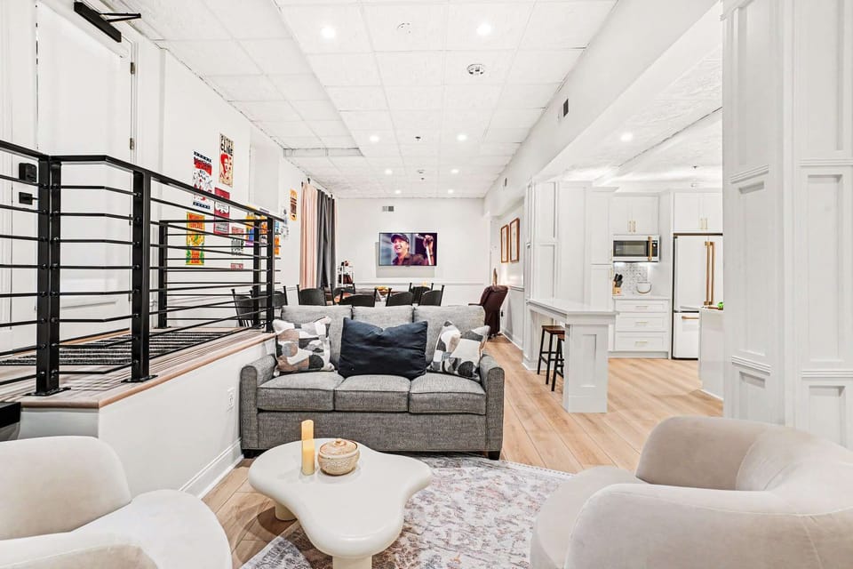 Relax in style in this bright living area, featuring a plush sofa, cozy swivel chairs, and a mounted TV, all open to the sleek white kitchen. Perfect for movie nights or casual conversation.