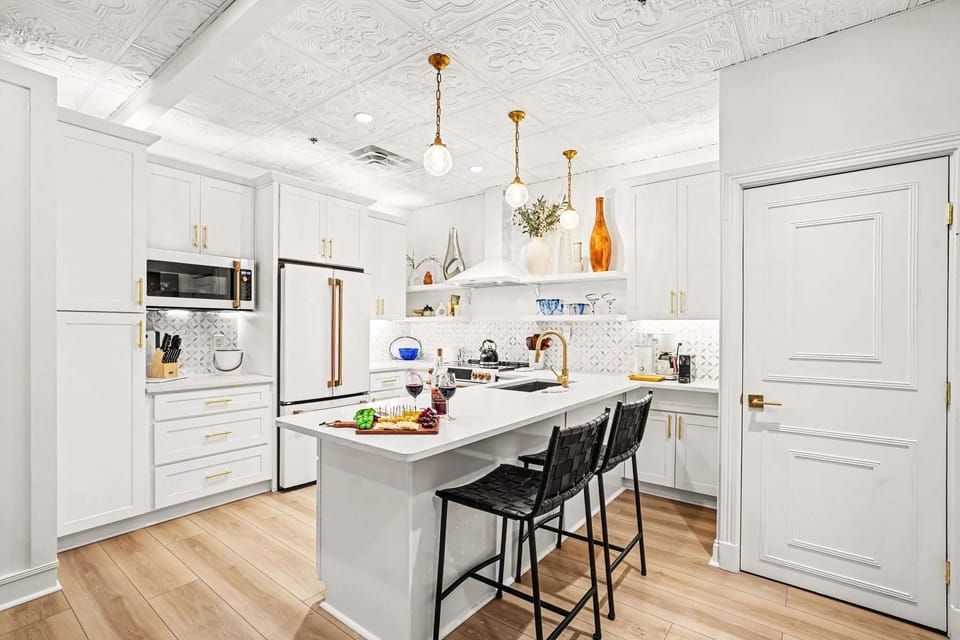 This white kitchen shines with brass and gold accents, high-end appliances, and an oversized island perfect for entertaining, all under a stunning pressed-tin ceiling for character.