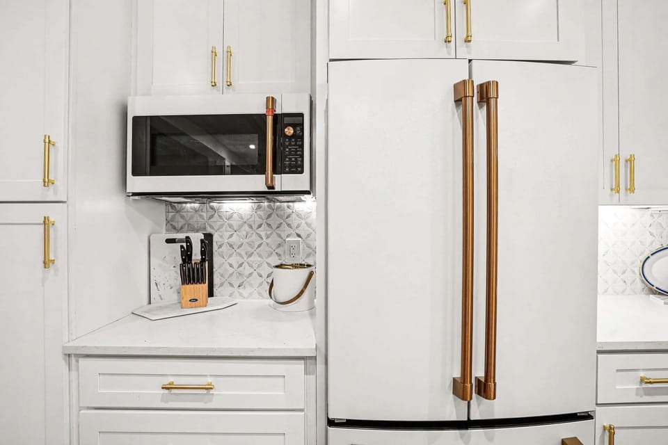 This white kitchen shines with brass and gold accents, high-end appliances, and an oversized island perfect for entertaining, all under a stunning pressed-tin ceiling for character.