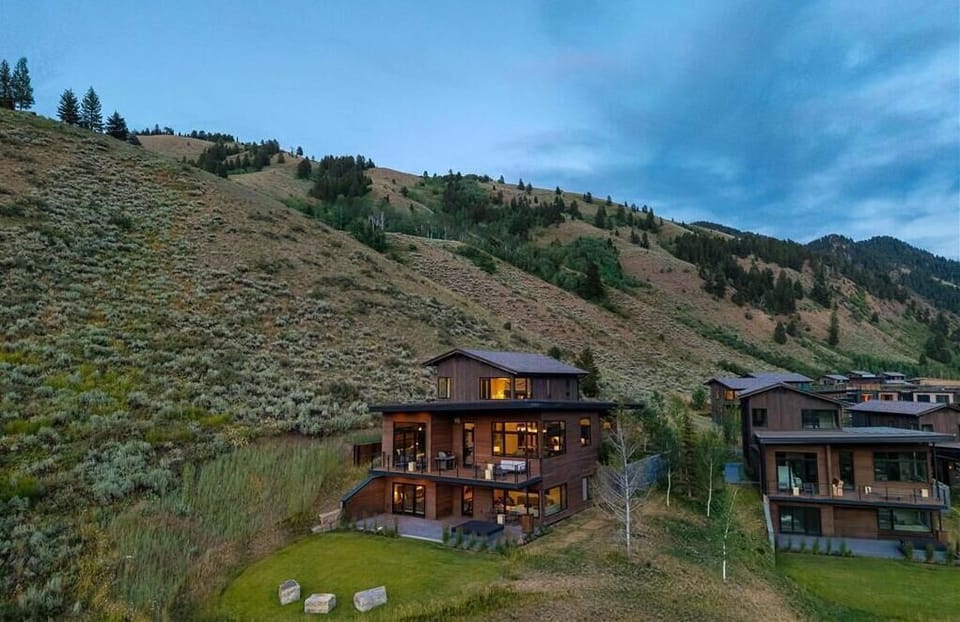 Cabin exterior at dusk, set among the hillside with warm light glowing through the windows