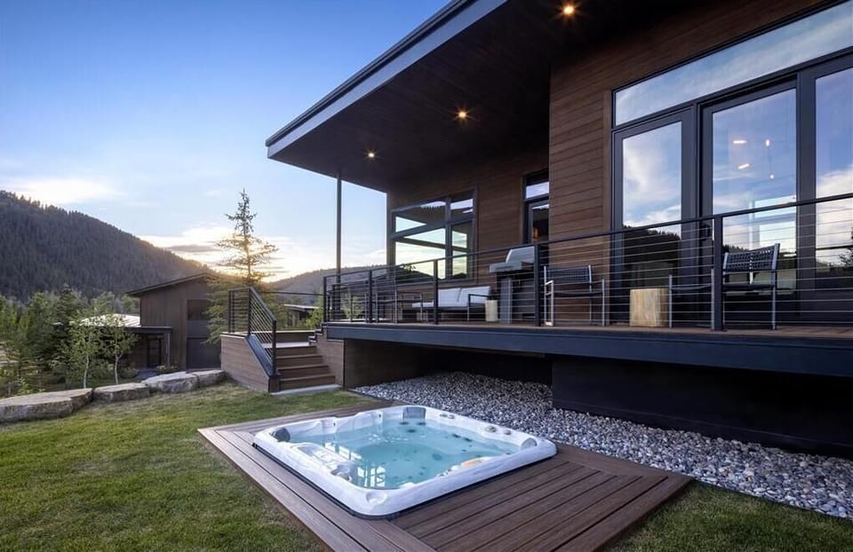 Cabin exterior with a deck and hot tub set against a densely forested hillside