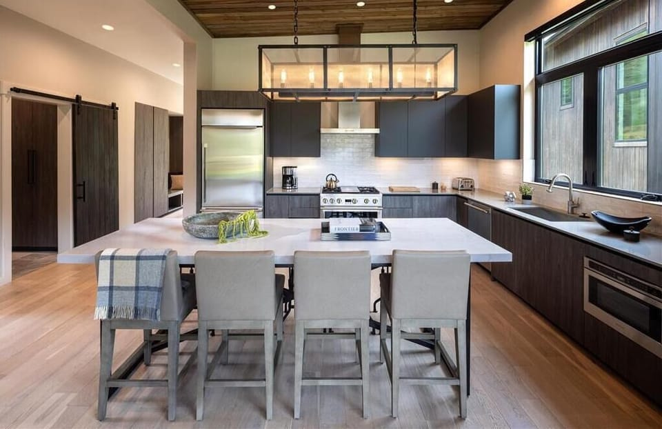Kitchen with dark cabinetry, a sliding barn door, and a six-seat island beneath wood-beam ceilings