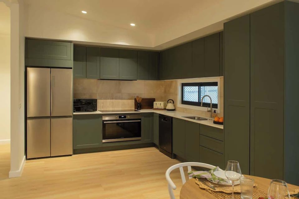 Cook with delight in this modern kitchen, featuring rich olive green cabinetry, stainless steel appliances, light hardwood floors, and crisp white countertops.