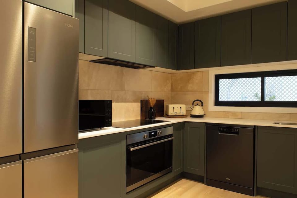 Create culinary delights in this modern kitchen, featuring rich olive green cabinetry, stainless steel and black appliances, white countertops, and warm ambient lighting.