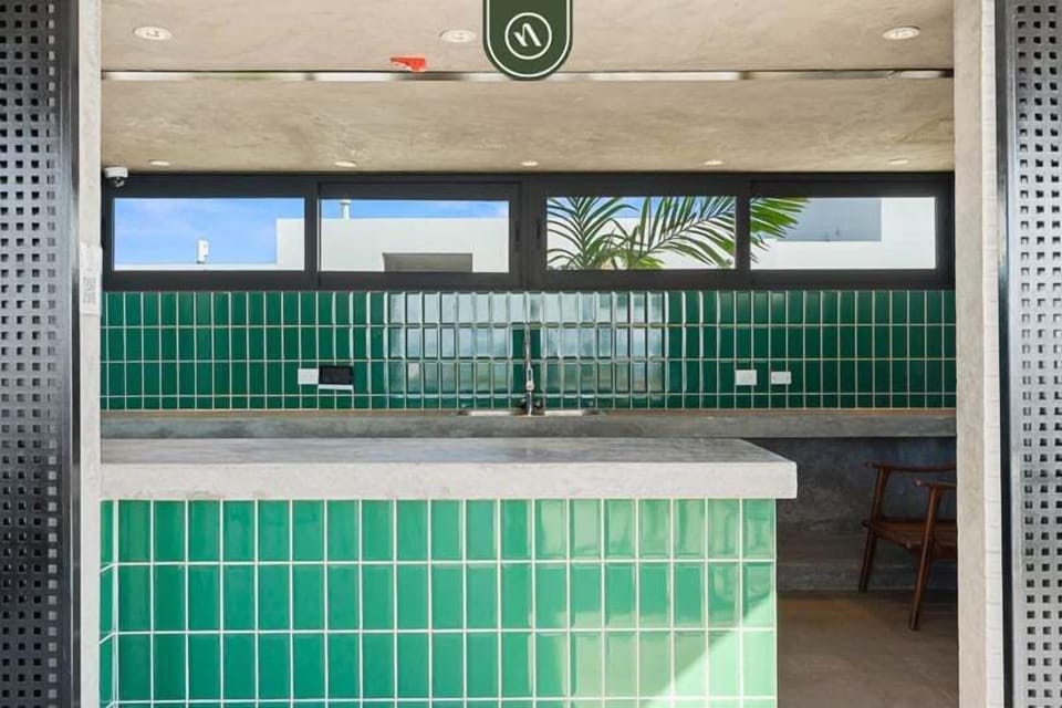 This vibrant rooftop bar and kitchenette area features striking green tile work, polished concrete countertops, an integrated sink, and sliding security screens for effortless outdoor hosting.