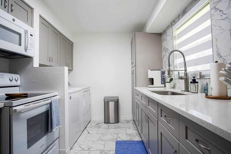 Bright, modern kitchen entry with spacious counters, touchless trash can, and an easy, functional layout for cooking and prep.