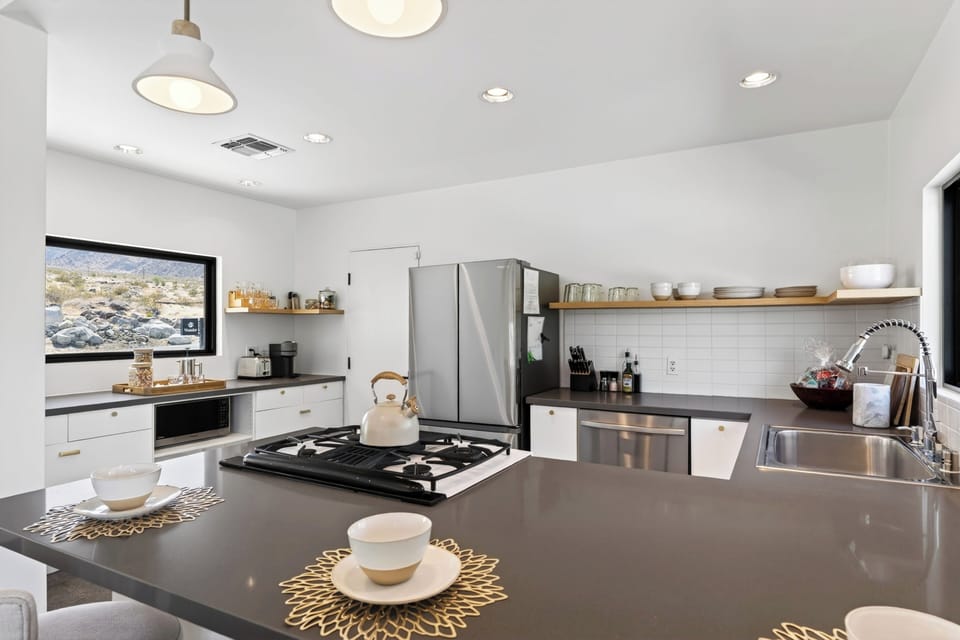 Chef’s kitchen equipped with a gas cooktop, stainless steel appliances, and minimalist open shelving.