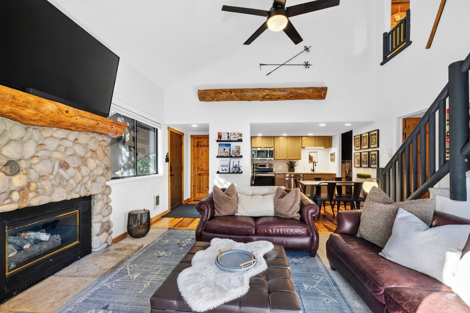 Cozy, open-concept living room featuring dark leather sofas, a stone fireplace, and vaulted ceilings.