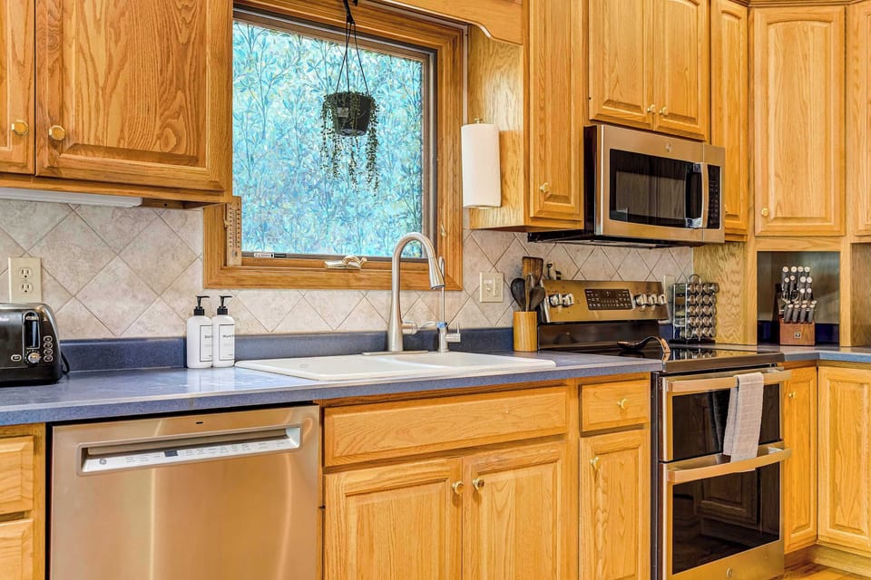 A window above the sink brings in soft natural light, framed by oak cabinetry on either side. Stainless appliances, including a built-in dishwasher and oven, sit beneath deep blue countertops for a clean, functional layout.
