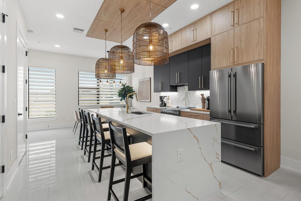 Your culinary haven awaits. Sleek marble counters, warm wood cabinetry, and woven pendant lights create an inviting space where preparing meals becomes a pleasure and gathering feels effortless.
