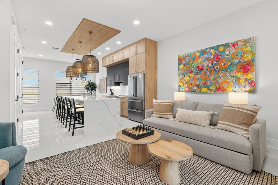 Settle into your bright open-plan living area, where sleek design meets coastal comfort. Cook in a modern kitchen with gleaming countertops, unwind on the sofa, and enjoy vibrant artwork that makes the space feel like home.