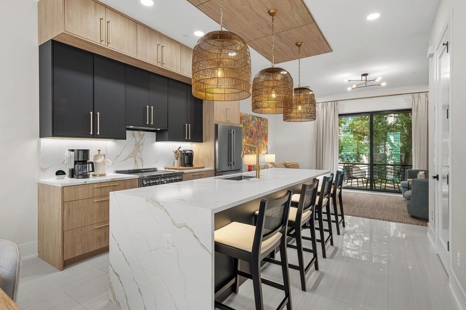 Gourmet kitchen featuring a marble waterfall island, woven pendant lights, and modern appliances—perfect for gathering with family or preparing meals in this bright, beautifully designed space.
