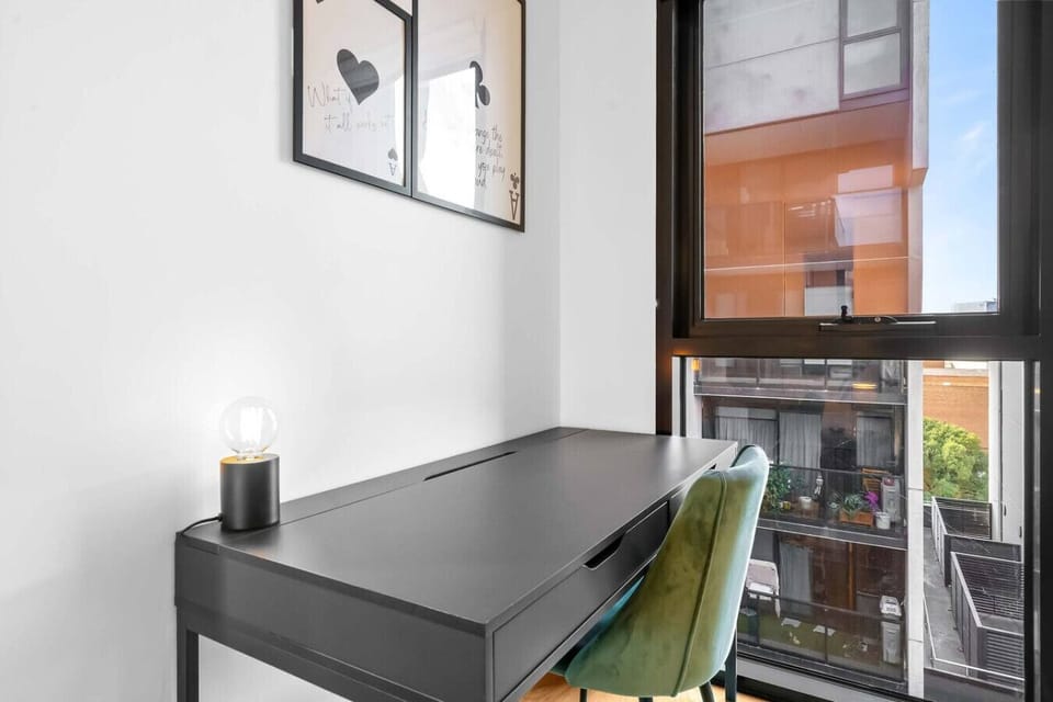 Compact workspace with a sleek dark desk, velvet chair, and city-facing window. A thoughtful setup for guests who need to stay connected or get work done during their stay.  *(172 characters)*