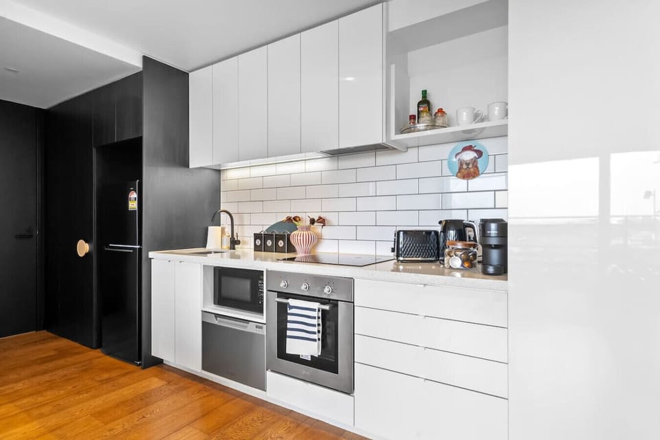 Bright modern kitchen with sleek cabinetry, tiled backsplash, and generous counter space. Fully equipped with cooktop, oven, microwave, kettle, toaster, and coffee machine, making it easy to prepare meals and enjoy a comfortable stay.