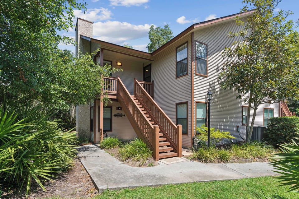 A cozy retreat nestled among lush greenery and mature trees, with a welcoming stairway leading to your home away from home on a peaceful, sunny afternoon.