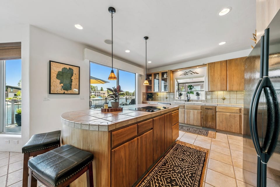 Your waterfront kitchen invites culinary creativity with its warm wood cabinetry, stylish tile counters, and views stretching across the shimmering water beyond.