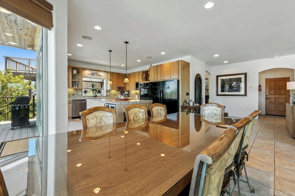 Gather around this spacious dining table where the warm wood tones and gleaming surfaces set the stage for your vacation meals together, with the kitchen just steps away and sunlight streaming through the door.