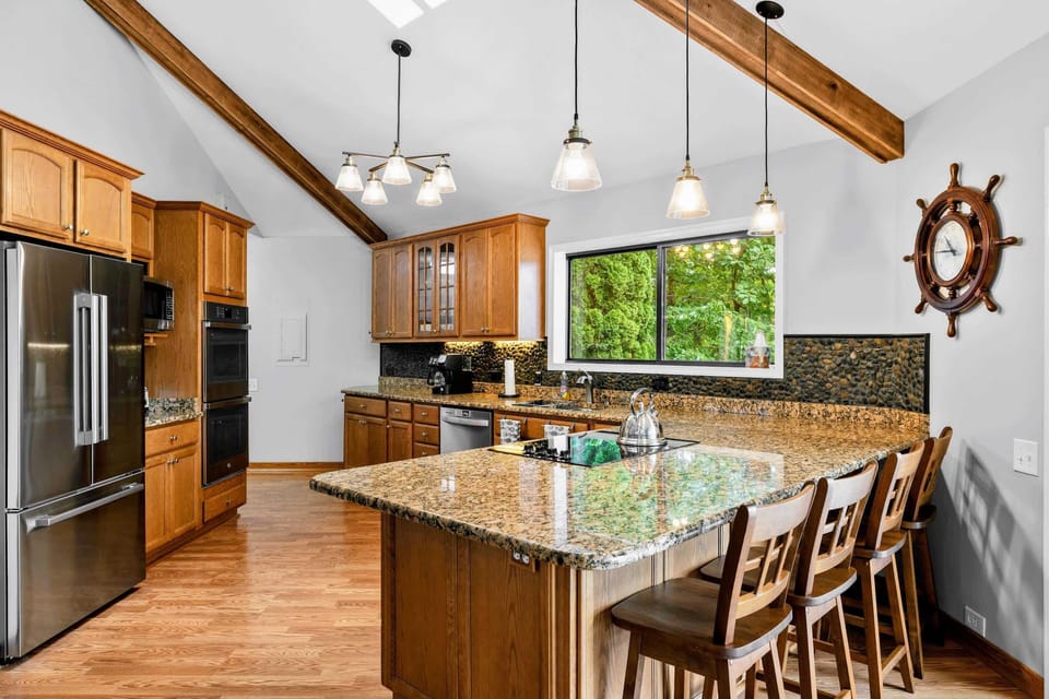 Kitchen - A granite peninsula with bar seating, stainless appliances, and vaulted beamed ceilings, open to the living space.
