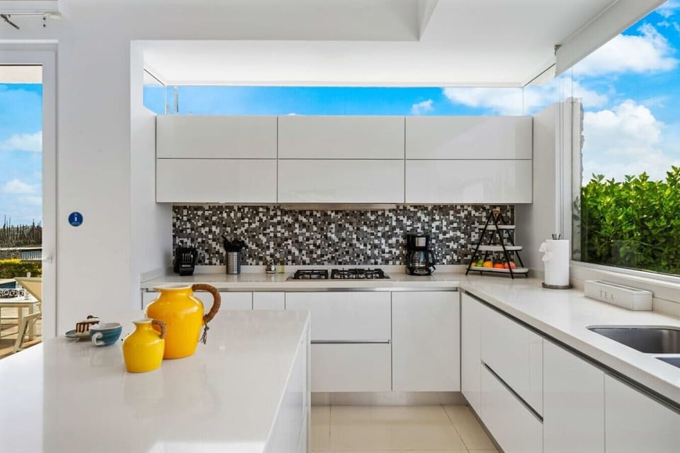 Cook, serve, and gather in a sleek modern kitchen where bright finishes and attractive views create an inviting setting for breakfasts, snacks, and shared meals.