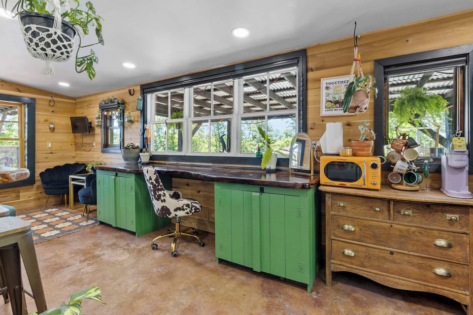 Ready Room - oversized desk, dishes, mini appliances (toaster oven, skillet, burner, microwave, and Keurig), small smart tv, couch, fridge, and oversized mirror with 3 stools. Wide view of the communal pavilion, cob oven, and play space