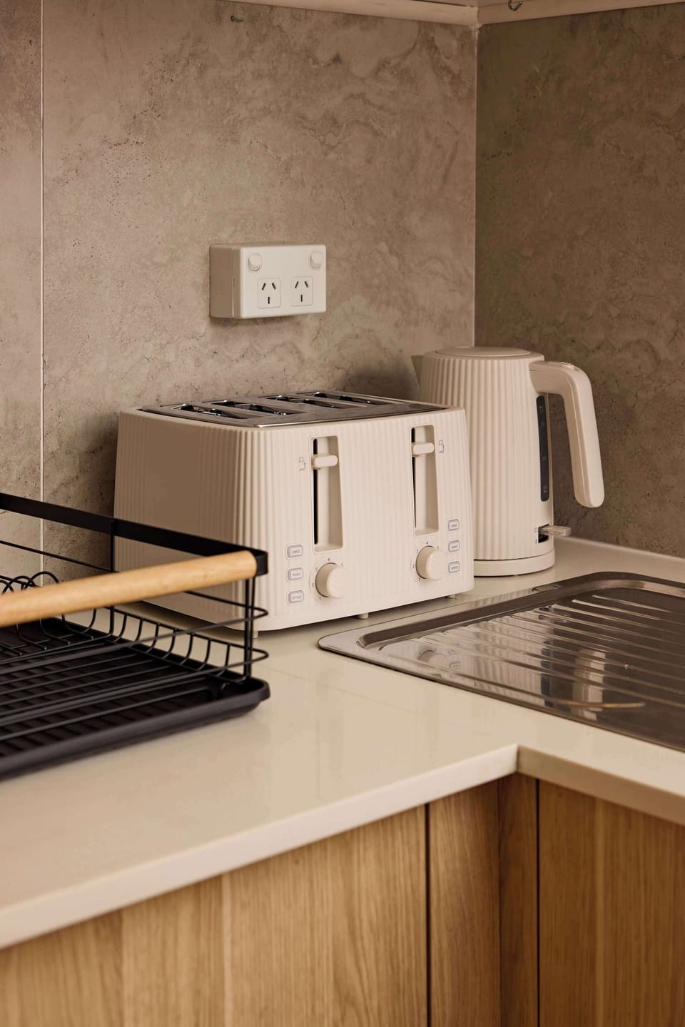 Enjoy convenient kitchen essentials, including a 4-slice toaster, electric kettle, and dish drying rack neatly arranged on sleek countertops next to light wood cabinetry.