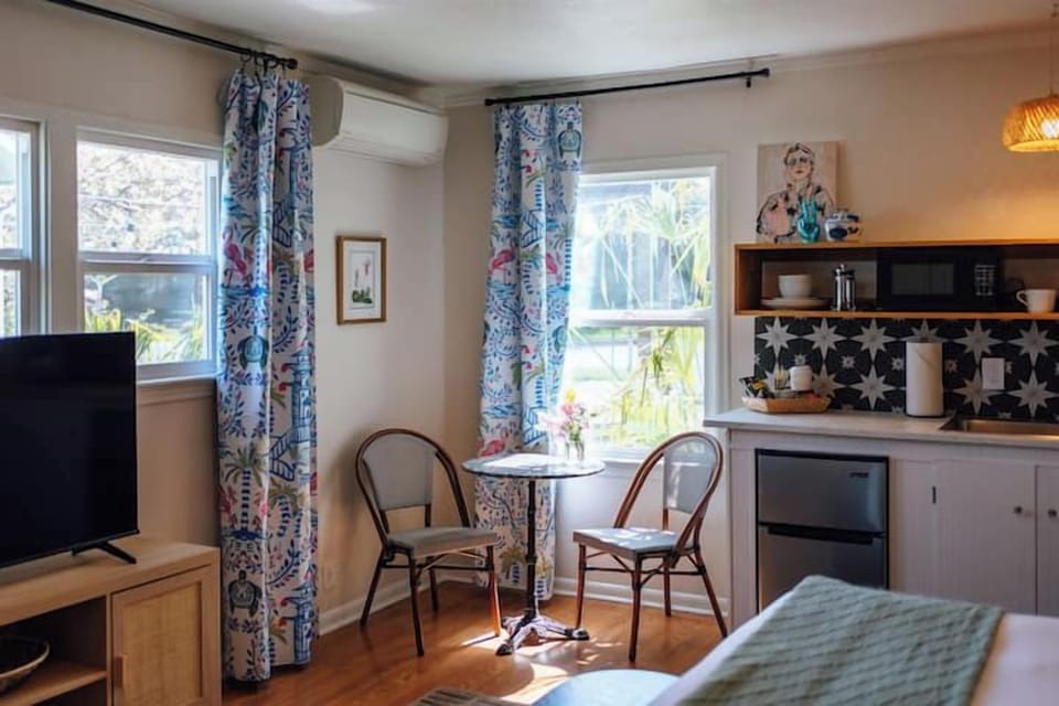 Swank 5: Charming studio seating area beside sunlit windows and a modern kitchenette setup.