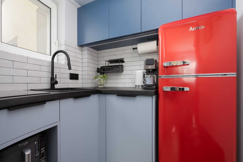 Modern kitchenette with blue cabinets, a retro-style red refrigerator, subway tile backsplash, and all the essentials for preparing meals.