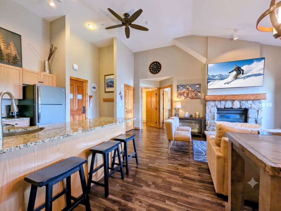 Unwind in your spacious open living area, where soaring vaulted ceilings, warm wood floors, and a cozy stone fireplace create the perfect mountain retreat. The granite-topped kitchen flows seamlessly into your comfortable lounge space.