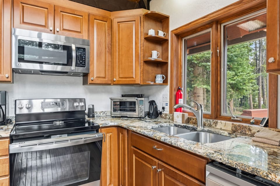 Your fully equipped kitchen features granite countertops, stainless steel appliances, and a view of the surrounding pine forest—perfect for preparing meals while soaking in the natural scenery.