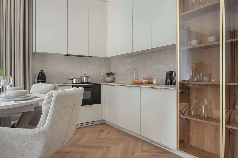 A linear kitchen workspace features off-white upper cabinets and matching lower units. Built-in appliances include a black induction cooktop and oven.