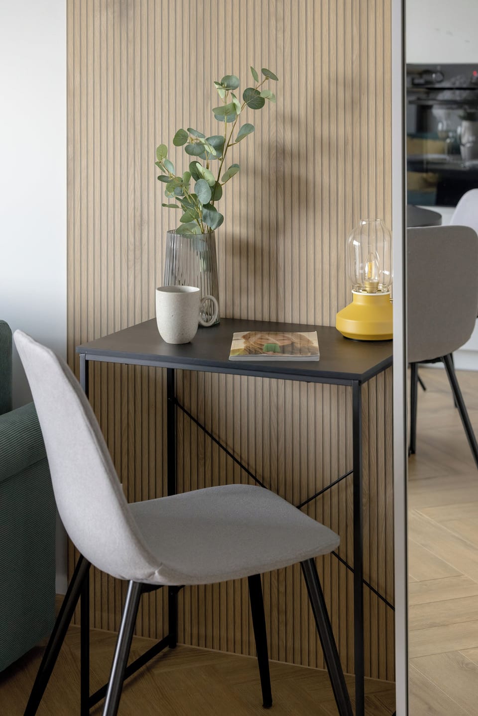 A detailed view captures the compact study desk paired with a light grey chair. A green glass vase with foliage decorates the small workspace.