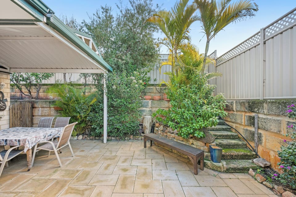 Relax and unwind in this private, paved courtyard featuring a covered patio, tiered garden beds, and lush tropical greenery.