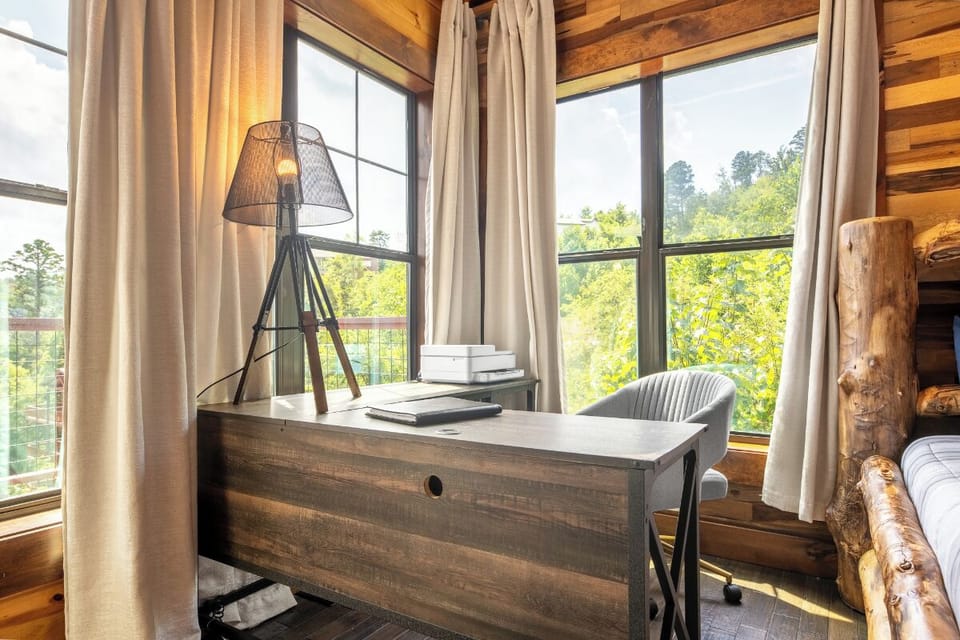 Settle in at your rustic workspace, where floor-to-ceiling windows frame lush treetop views and natural light floods the warm wood-paneled room. Your perfect hideaway for inspired mornings.