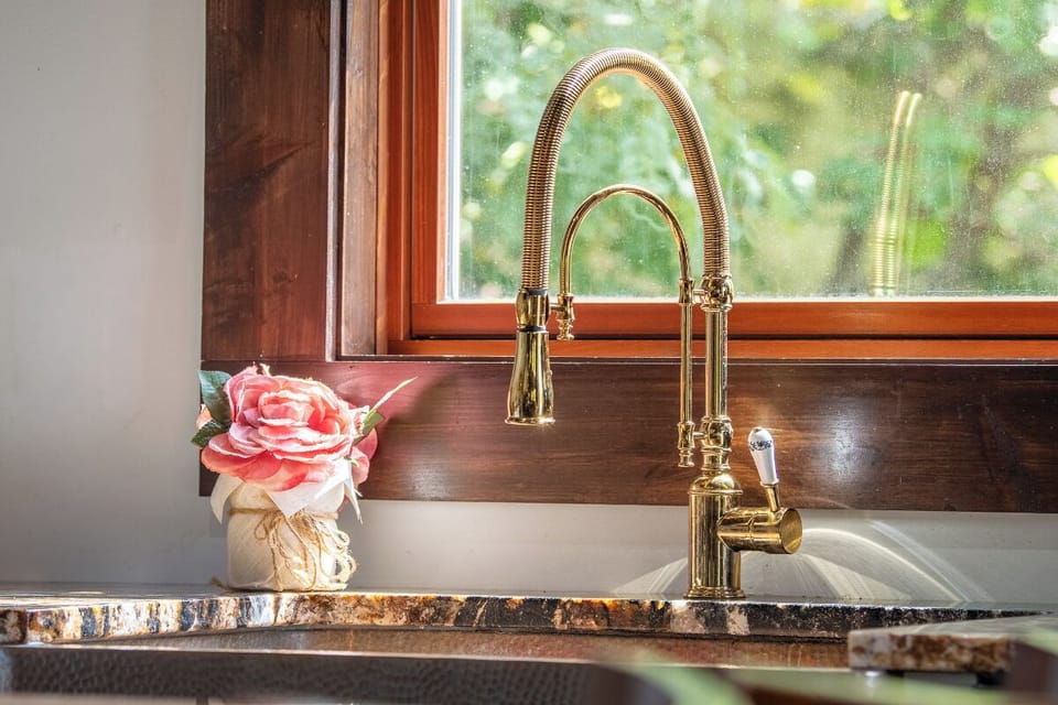 You'll love preparing meals at your elegant brass faucet, framed by warm wood tones and soft natural light streaming through the window above your sink.