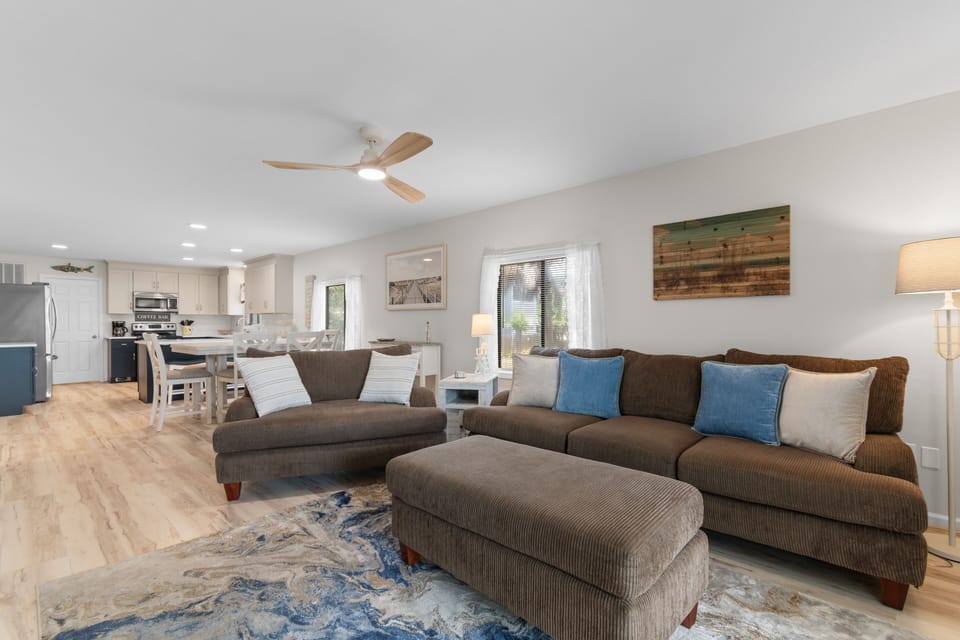 Open living room with two sofas, ottoman, ceiling fan, and view through to kitchen at Ocean Bliss Unit 102, Surfside Beach
