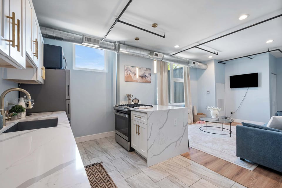 Combined kitchen and living area with marble-look counters, mounted TV, and blue sofa. Open layout keeps the group connected whether cooking or relaxing.
